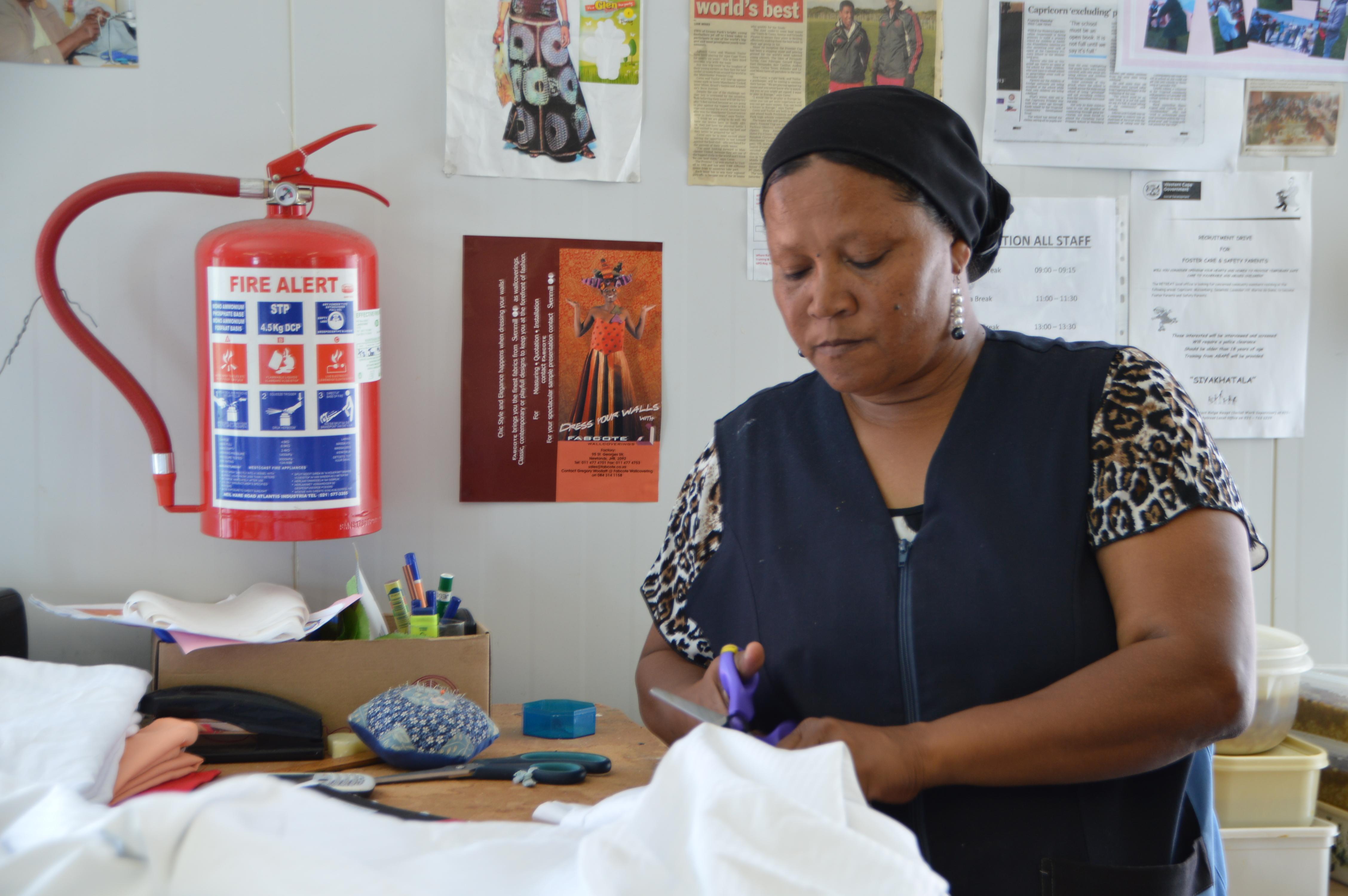 Como parte de su pasantía de desarrollo internacional en Sudáfrica, pasante ayuda a preparar materiales. Female International Development Intern cuts with scissors through material during her work placement in South Africa.